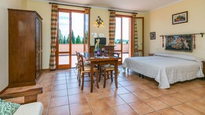 A room with a bed, a dining table with chairs, a wooden wardrobe, and a balcony with curtains. - Nice apartment for 2 guests with WIFI, A/C, pool, TV and pets allowed (Cerreto Guidi)
