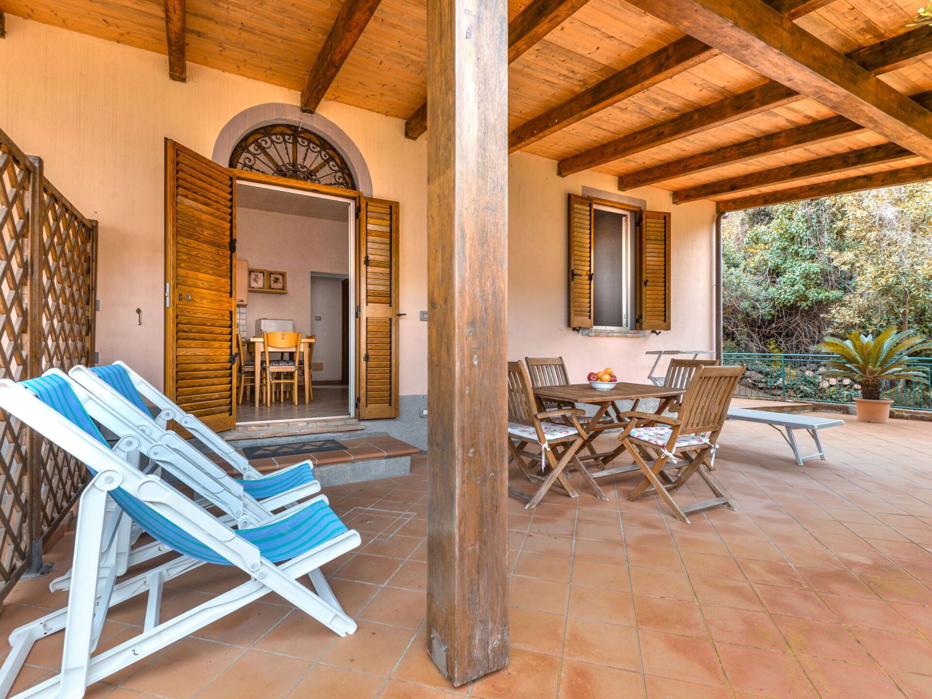A covered patio with wooden furniture, a dining table with chairs, and a view of the garden.
