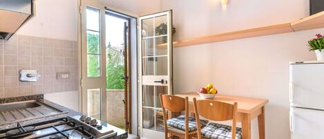 Una cocina con estufa a gas, una mesa de comedor con sillas, un refrigerador y una ventana con vistas al verdor.