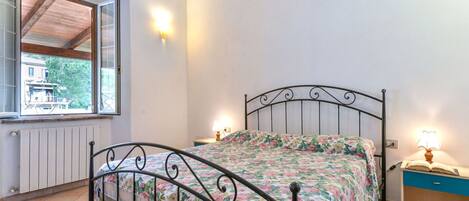 Un dormitorio con estructura de cama metálica, ropa de cama floral, una ventana con vistas y lámparas de noche.