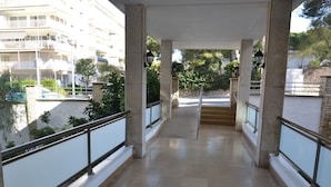 Un balcon couvert doté d’un sol carrelé, de rampes en métal et offrant une vue sur un bâtiment et la verdure en arrière-plan.
