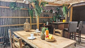 A wooden deck with a bar area, a table set with a pineapple, fruit, and drinks, and a sign that reads "BAR". - Beautiful  villa for 3 people with WIFI, TV and patio (Petit Saint-malo)
