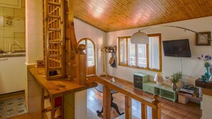 Interior de madera con una escalera, una zona de cocina y una sala de estar con televisor.