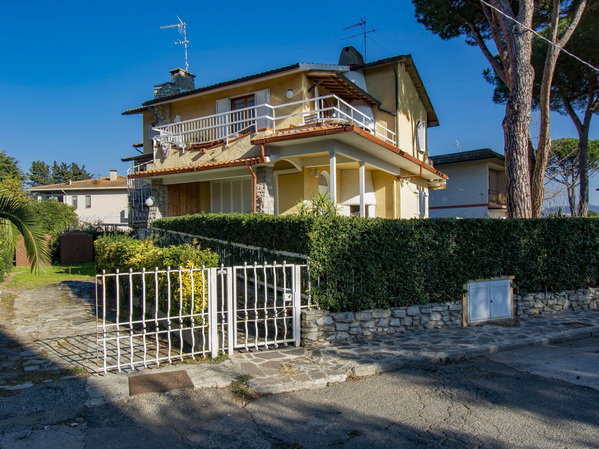 A two-story house with a balcony, stone wall, and a gate.