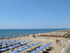 A beach with rows of blue umbrellas and sun loungers, a lifeguard tower, and a clear view of the sea.
