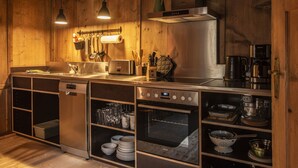 A modern kitchen with wooden walls, stainless steel appliances, and hanging utensils. - Cosy apartment in villa for 8 guests with WIFI and terrace (Kauns)