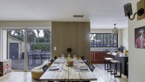 Un coin repas avec une longue table en bois, dressée pour six personnes, entourée de chaises noires. Une grande fenêtre offre une vue sur l’extérieur.