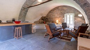 A cozy kitchen with a stone arch, a wooden bar, and a seating area with chairs and a table.