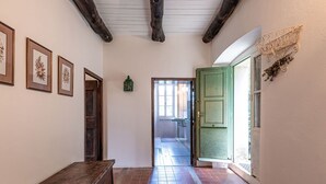 A hallway with a wooden bench, framed botanical prints on the wall, a green door, and a rustic ceiling.
