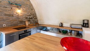 A kitchen with a stone wall, wooden countertop, stainless steel appliances, and a red sink.