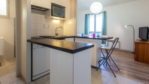 Ett kompakt kök med mikrovågsugn, diskho och en liten matplats med en stol och ett bord.