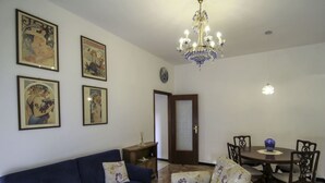 A living room with a blue sofa, floral armchair, wooden coffee table, and a dining area with a table and chairs.