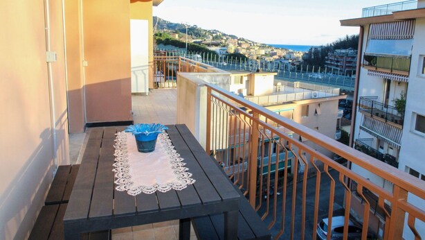 A balcony with a table and chairs, overlooking a cityscape with buildings and a body of water.