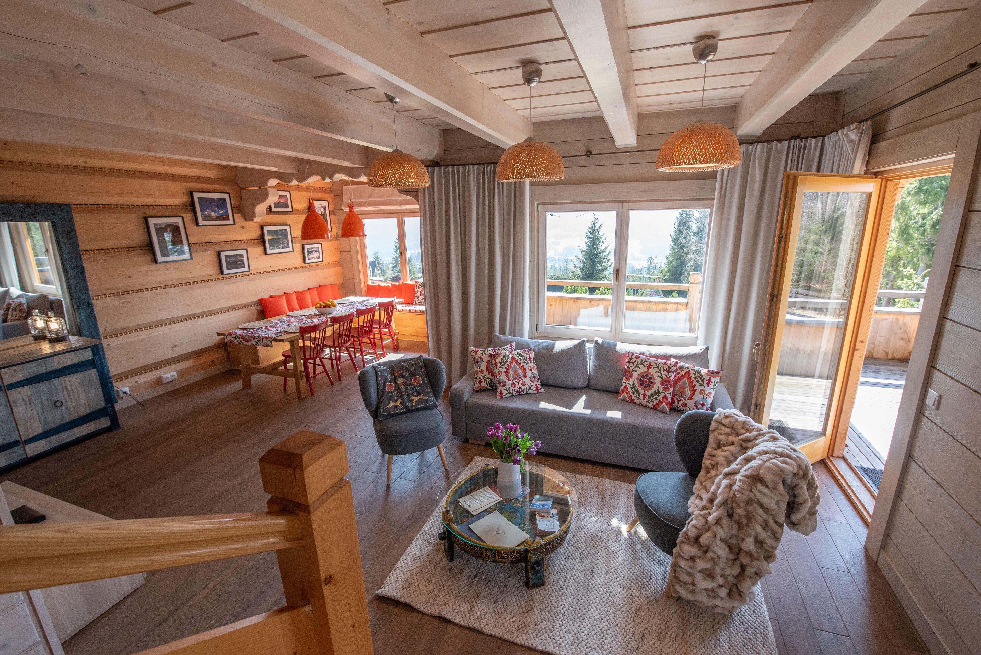 Interior acogedor de una cabaña con detalles de madera, un sofá, zona de comedor y un ventanal con vistas al exterior.