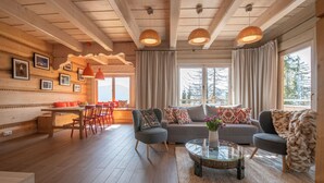 Een knusse woonkamer met een houten plafond, een zithoek, een salontafel en een eethoek met stoelen en een tafel.