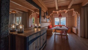 Een houten hut van binnen, met een eethoek, houten balken en een groot raam met uitzicht op bergen.