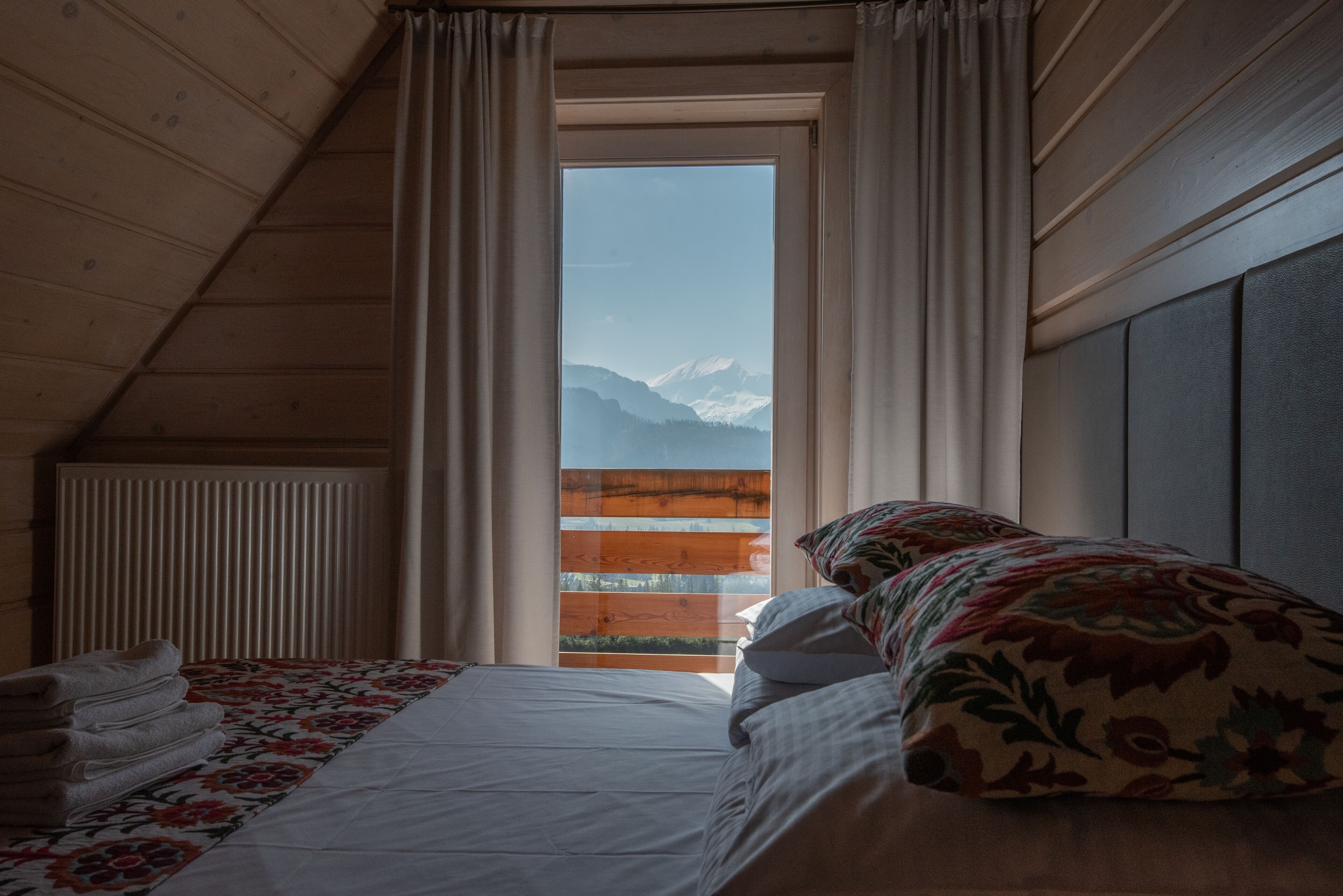 Un dormitorio con cama, una ventana con cortinas, un radiador y vistas a montañas.