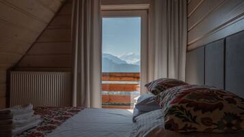 Un dormitorio con cama, una ventana con cortinas, un radiador y vistas a montañas.