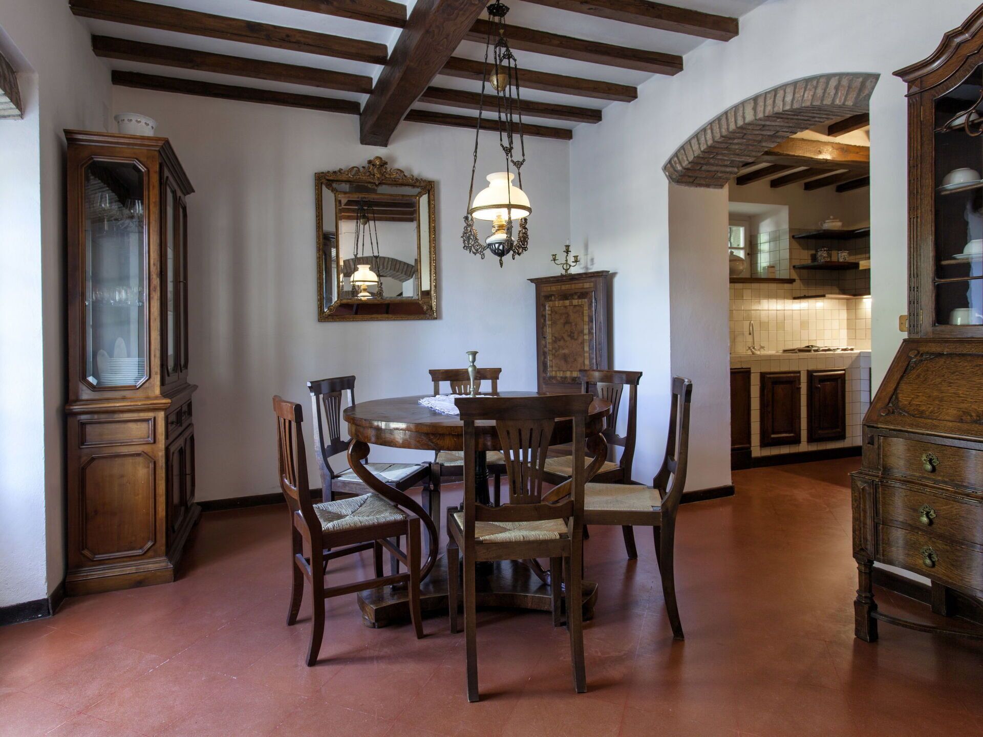 Un comedor con una mesa y sillas de madera, una lámpara de araña y un espejo grande en la pared.