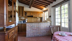 A rustic kitchen with wooden cabinets, a brick island, and a window with a view of greenery.