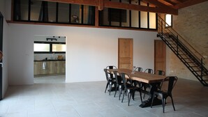 Een ruime eethoek met een houten tafel en stoelen, een keuken op de achtergrond en een trap naar een hoger gelegen verdieping.