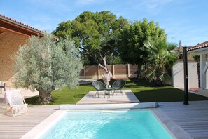 A backyard with a swimming pool, two lounge chairs, a small table, and a tree. - La Maison Bois Carré Idéale Pour des Vacances en Famille ou Entre Amis ! (Saint-Yzans-de-Médoc)