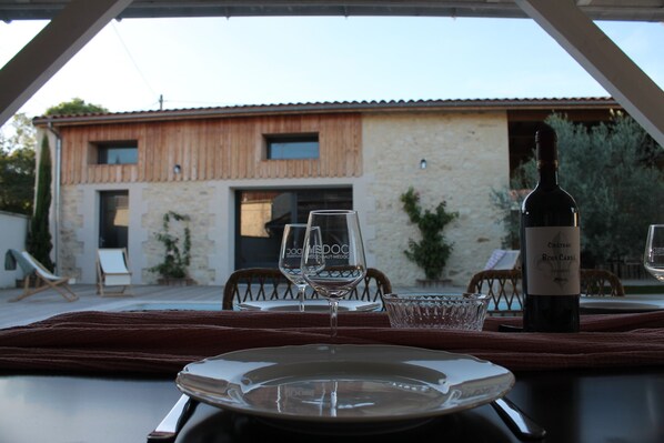 A dining table set with wine glasses and a bottle, with a view of a rustic building in the background.