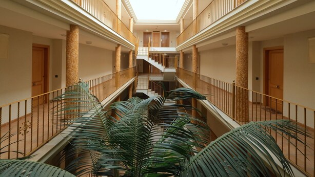 Een atrium met meerdere verdiepingen, een centrale trap, zuilen en potplanten.
