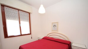 Ein Schlafzimmer mit einem Bett, einem Nachttisch, Vorhängen und einer Hängelampe.