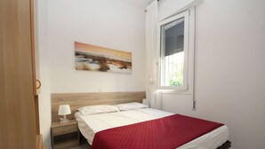 Ein Schlafzimmer mit Bett, Nachttisch, Lampe, einem Fenster mit Vorhängen und einem Bild an der Wand.