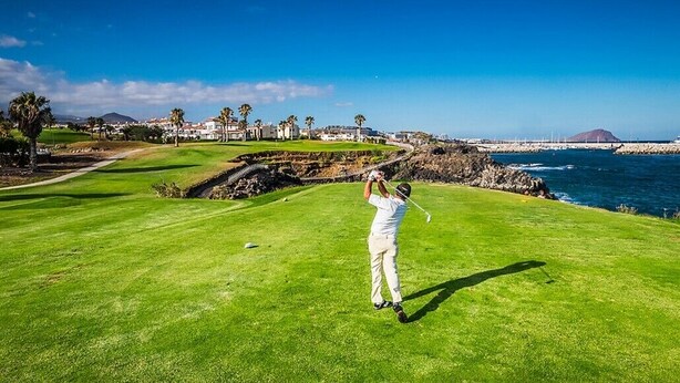 Een golfbaan met uitzicht op de oceaan en een bergachtige achtergrond.