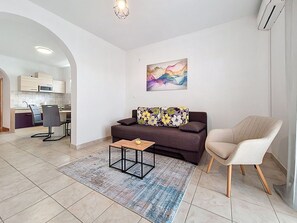A living room with a sofa, a coffee table, a chair, a rug, and a kitchen in the background.