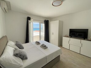 A hotel room with a bed, a TV, a wardrobe, and a view of the sea. - Cosy apartment for 4 guests with WIFI, A/C, TV and balcony (Zadar)