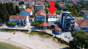 Ett flygbildsfoto av ett bostadsområde vid kusten med hus, en strand och en röd pil som pekar på en specifik plats.