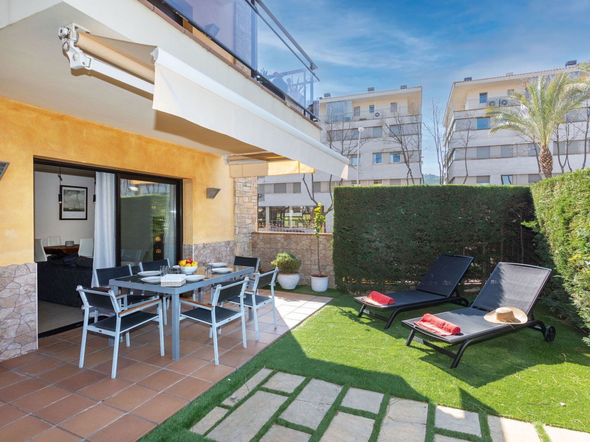 Um pátio externo com uma mesa de jantar e cadeiras, uma pequena área de jardim com um viveiro e vista para edifícios vizinhos.