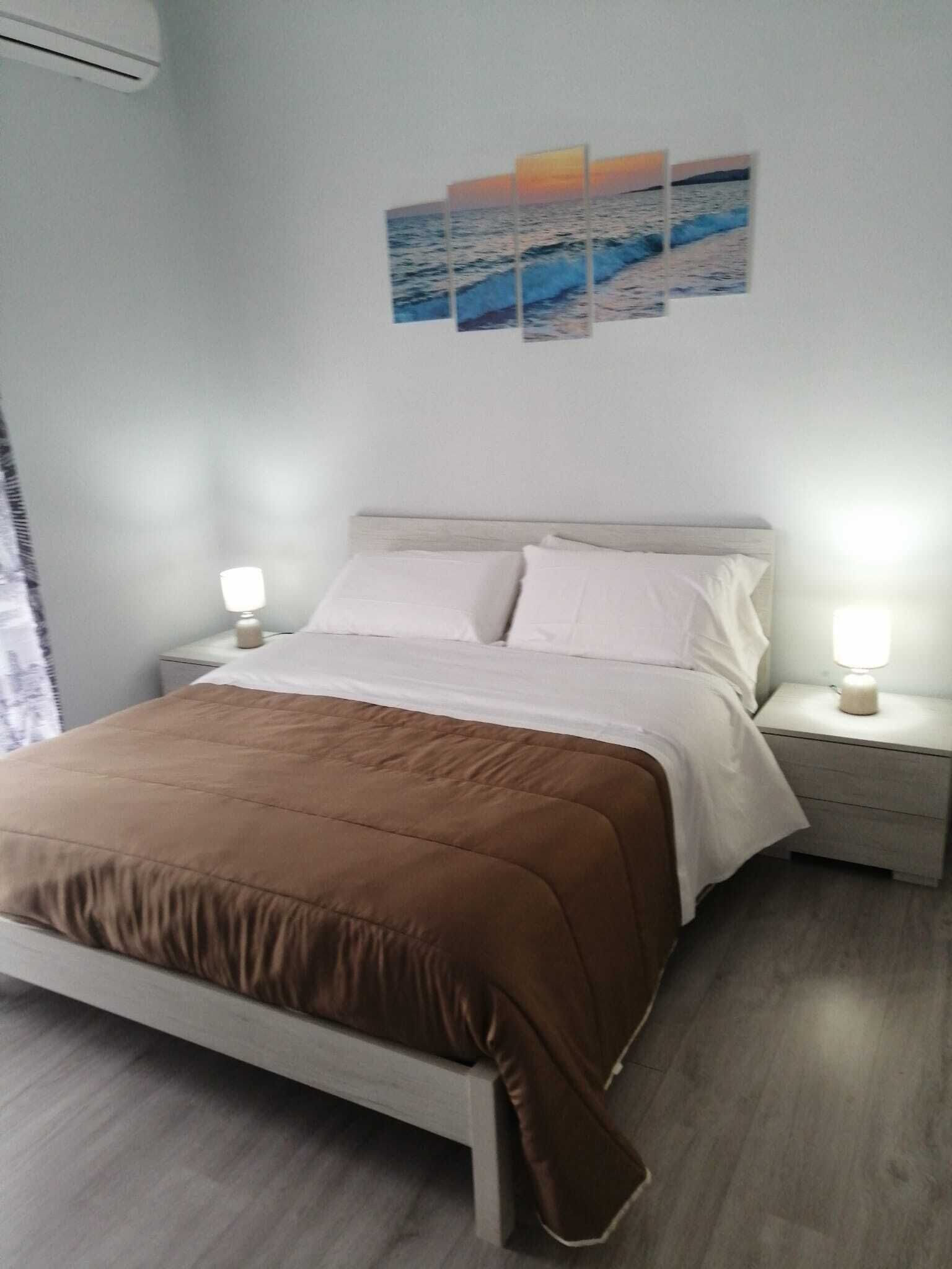 A bedroom with a bed, nightstands, a lamp, and a wall-mounted artwork.