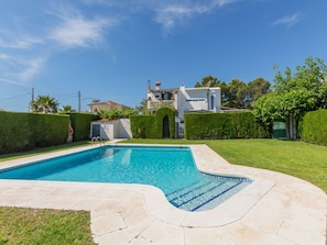 A swimming pool with a curved edge, surrounded by a well-maintained lawn and a hedge.
