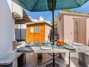 An outdoor dining area with a table set for four, a wooden structure, and a covered seating area.