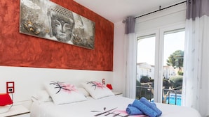Een hotelkamer met een bed, kussens, een nachtkastje, een rode lamp en een schilderij aan de muur.