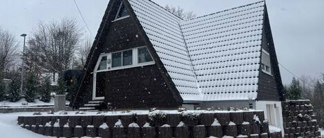 Une maison recouverte de neige, dotée d’un toit triangulaire original et d’un petit porche.