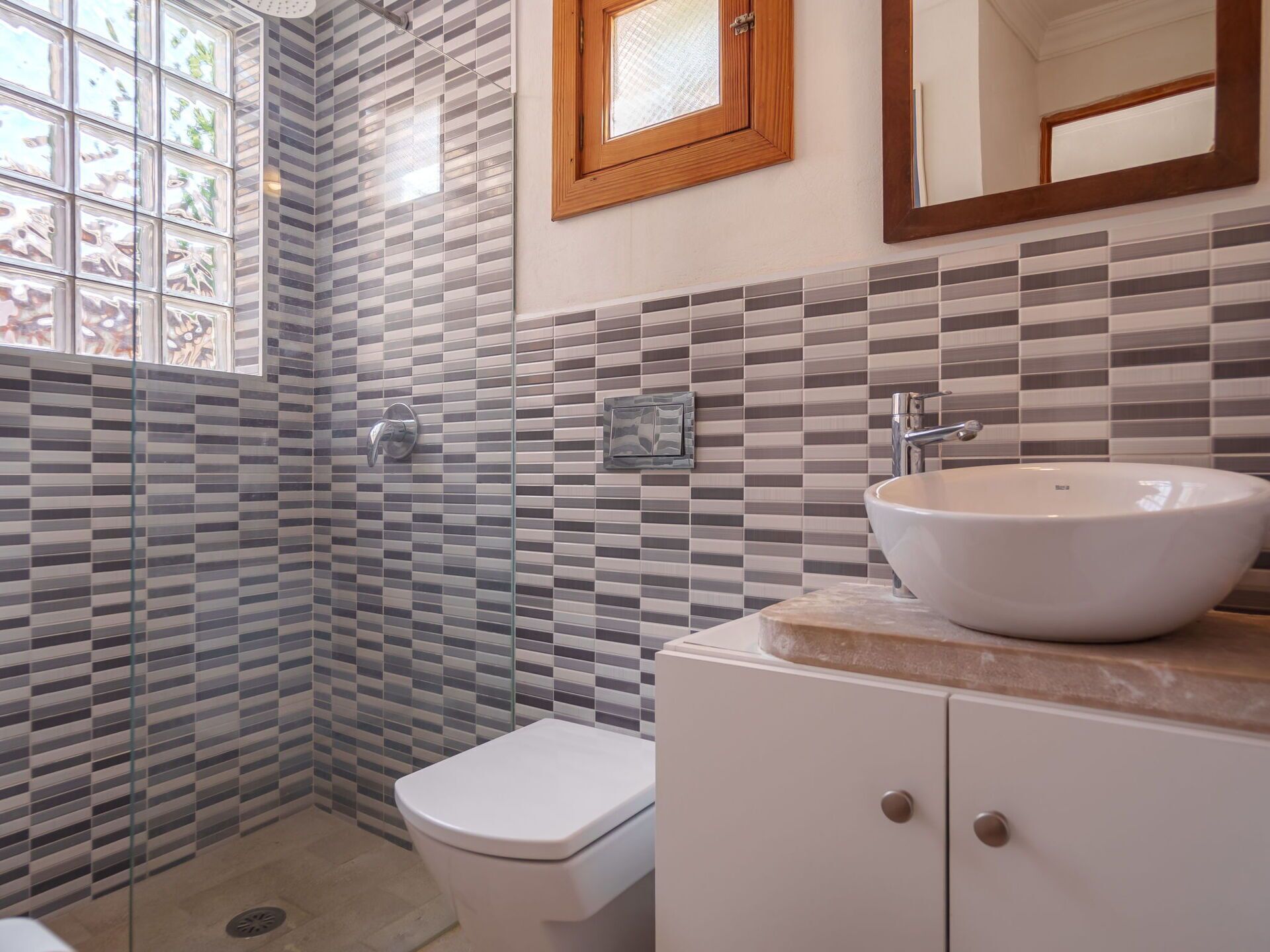 A bathroom with a white toilet, a sink with a marble countertop, and a shower area with patterned tiles.