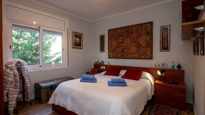 Ein Schlafzimmer mit einem großen Bett, einem Nachttisch, einem roten Teppich und einem Fenster mit Blick auf Bäume.