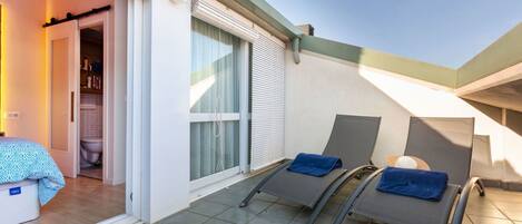 A balcony with two sun loungers, a door leading to a bathroom, and a tiled floor.