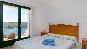 A bedroom with a bed, a nightstand, a lamp, and a view of the sea through a large window. - Wonderful private villa for 6 guests with pool, TV, terrace and panoramic view (L'escala)