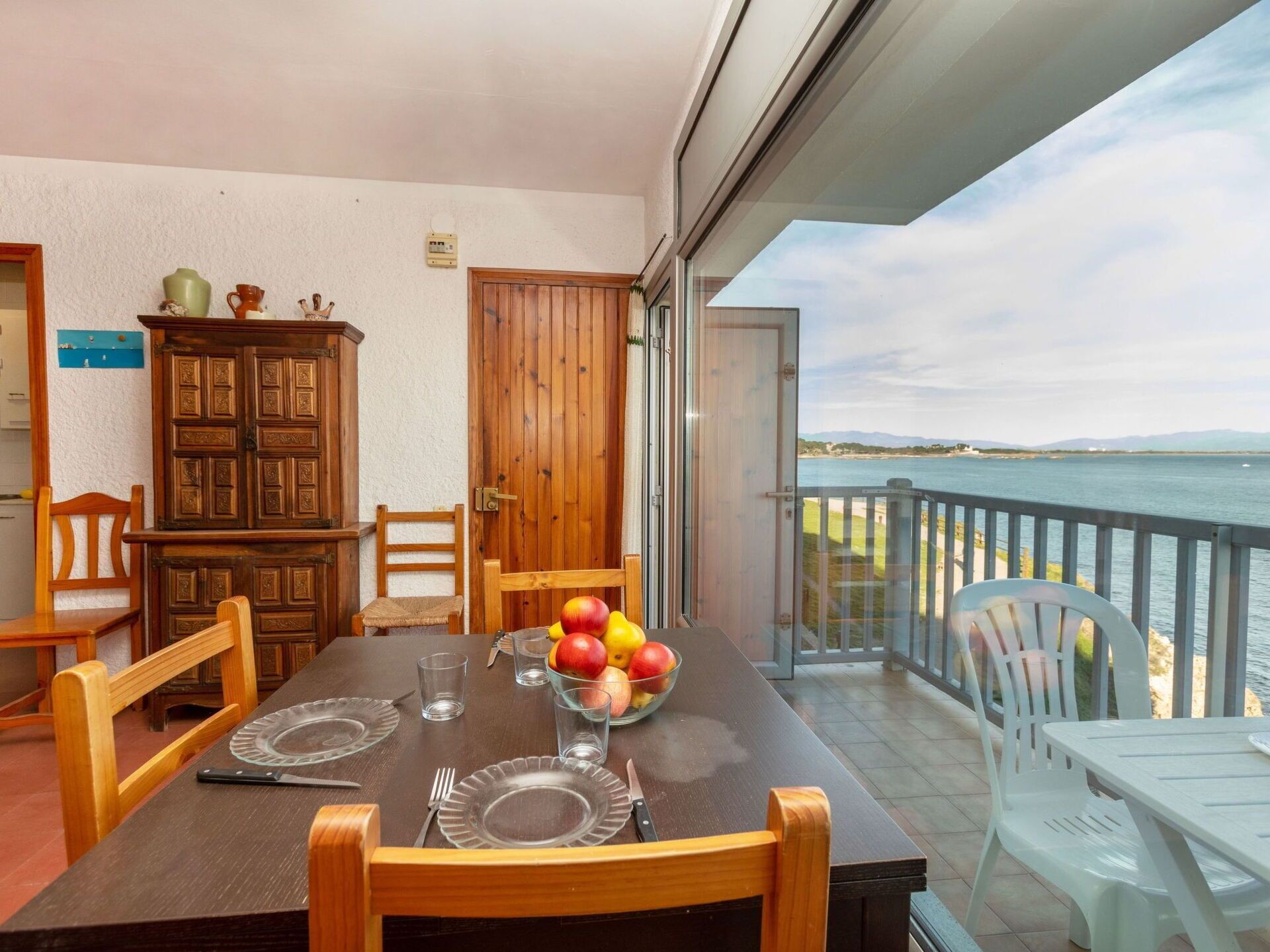 Un coin repas avec une table dressée pour quatre personnes, un buffet en bois et une vue sur la mer.