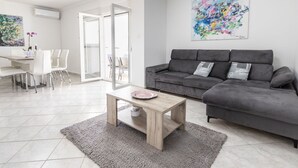 Een moderne woonkamer met een grijze bank, een houten salontafel en een eethoek met witte stoelen en een tafel.