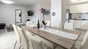 Een moderne, goed verlichte eetruimte met een houten tafel, witte stoelen en een keuken op de achtergrond.