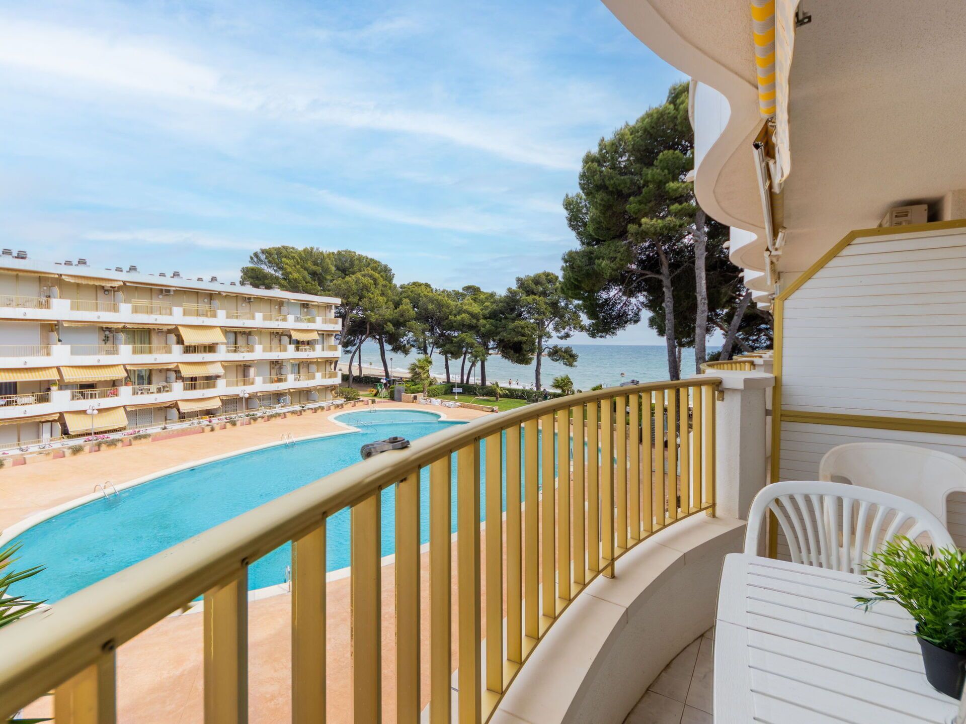 A hotel balcony with a pool, overlooking a beach and a building with multiple balconies.