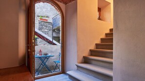 A staircase leading to a balcony with a table and chairs, a door leading outside, and a view of a stone building.