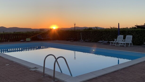 Ein Schwimmbecken mit klarem Wasser, umgeben von einer Ziegelterrasse und weißen Liegestühlen.